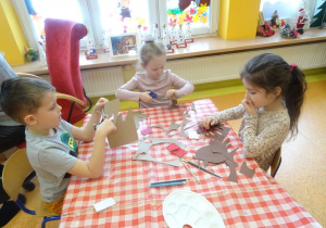 Trójka dzieci wycina szablon dłoni z papieru.